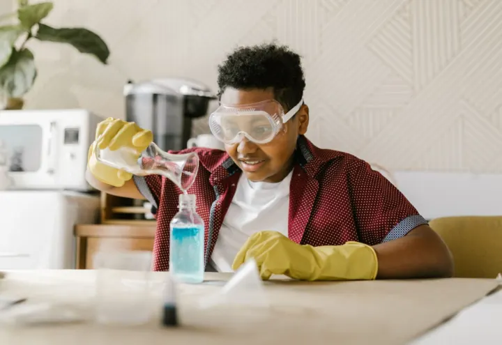 Boy in safety goggles pouring liquid into a bottle during a science experiment