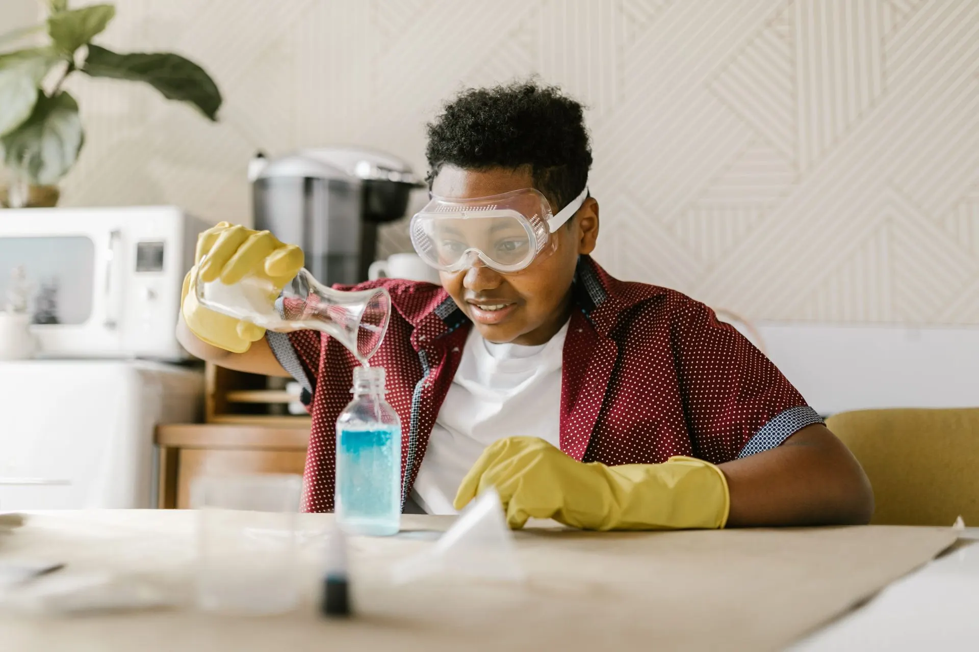 Boy in safety goggles pouring liquid into a bottle during a science experiment
