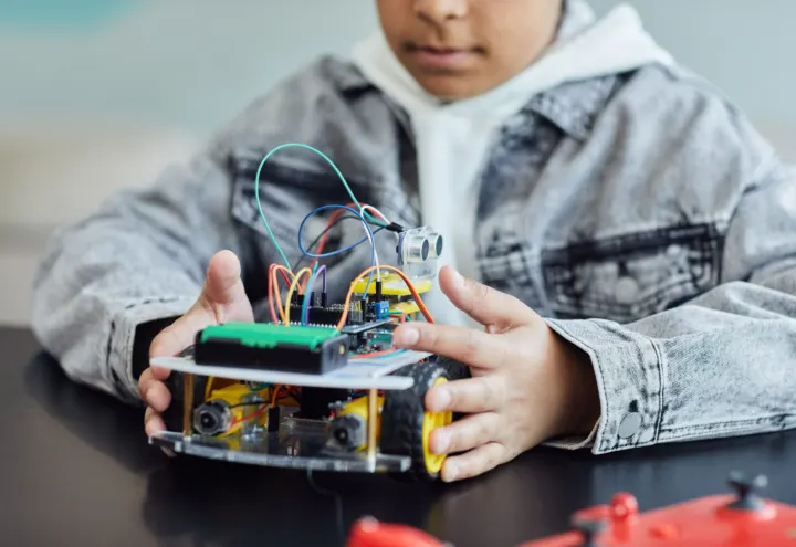 Child holding a hand-built robot car kit with sensors, wires and yellow wheels