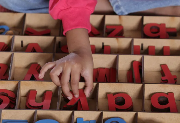 Child picking red wooden letters from a Montessori movable alphabet box