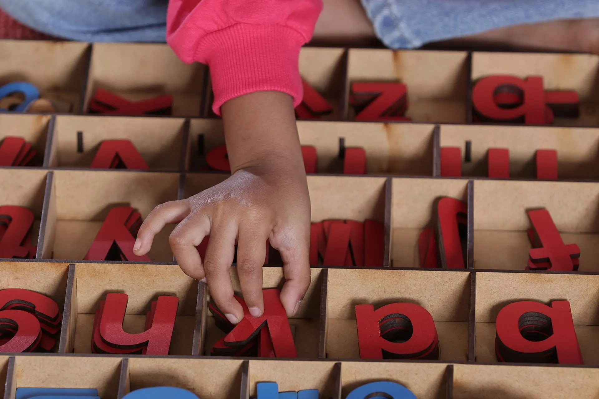 Child picking red wooden letters from a Montessori movable alphabet box