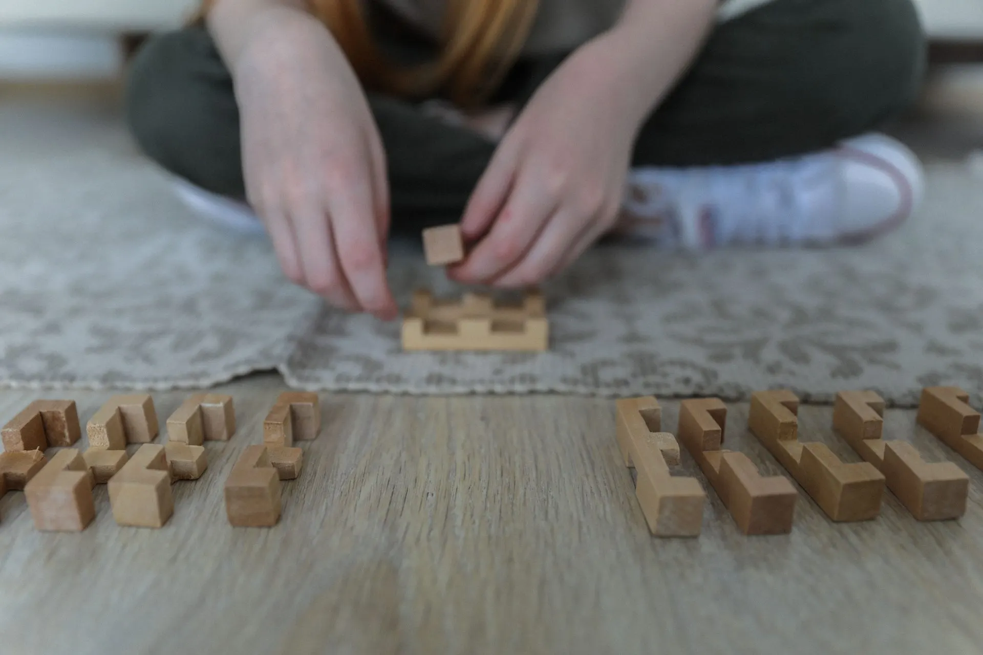 Child sitting cross-legged on a rug fitting together small wooden building blocks