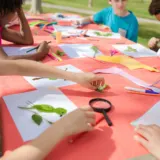 Children making leaf collages with paper, pencils and glue at an outdoor craft table