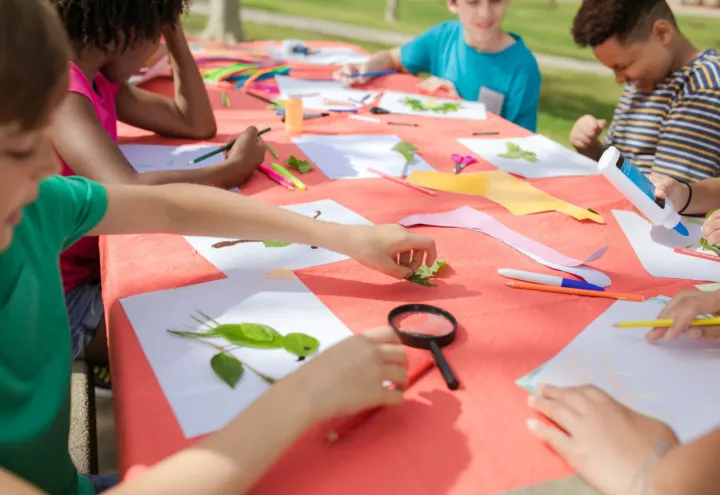 Children making leaf collages with paper, pencils and glue at an outdoor craft table