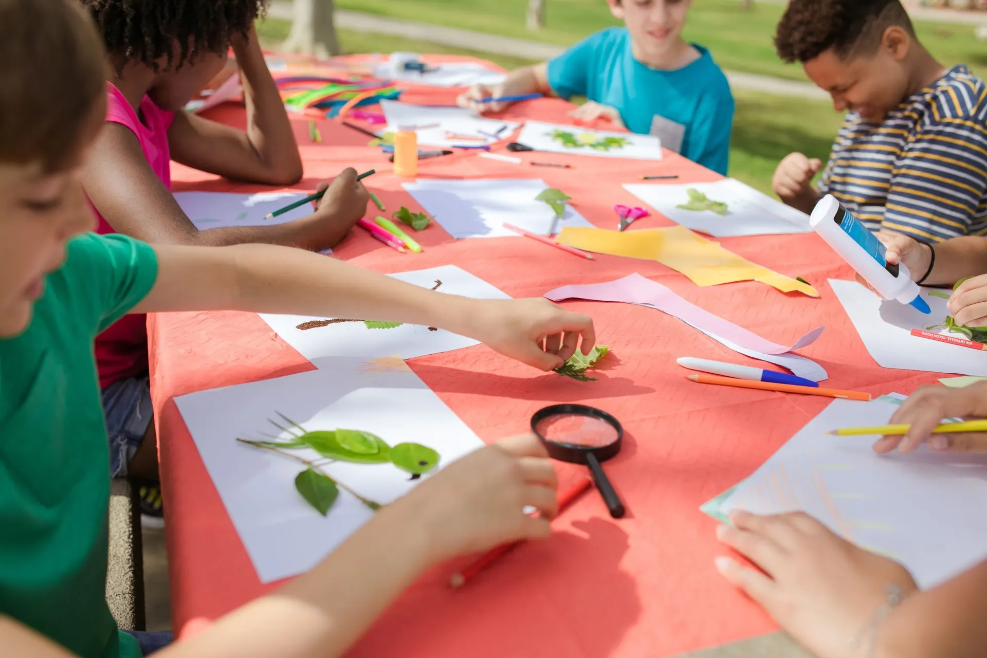 Children making leaf collages with paper, pencils and glue at an outdoor craft table