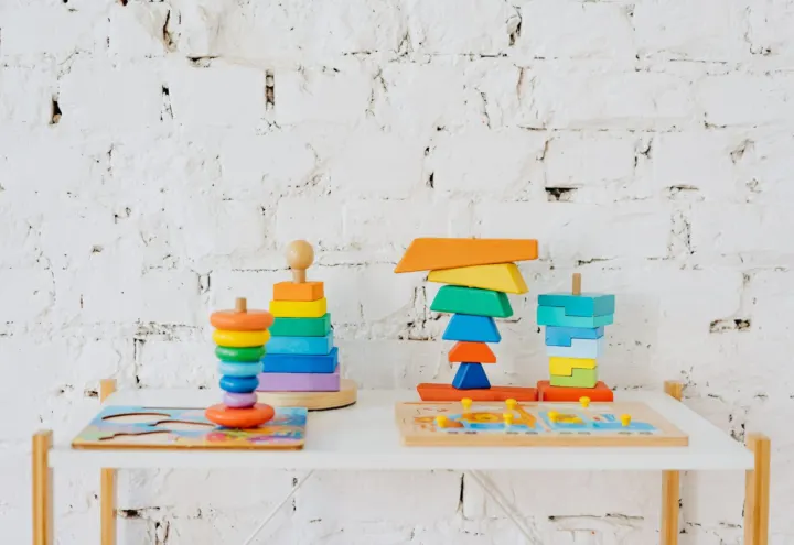 Colorful wooden stacking toys and peg puzzles on a small white table against brick