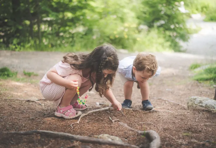 Girl and toddler crouching on a forest path exploring tree roots