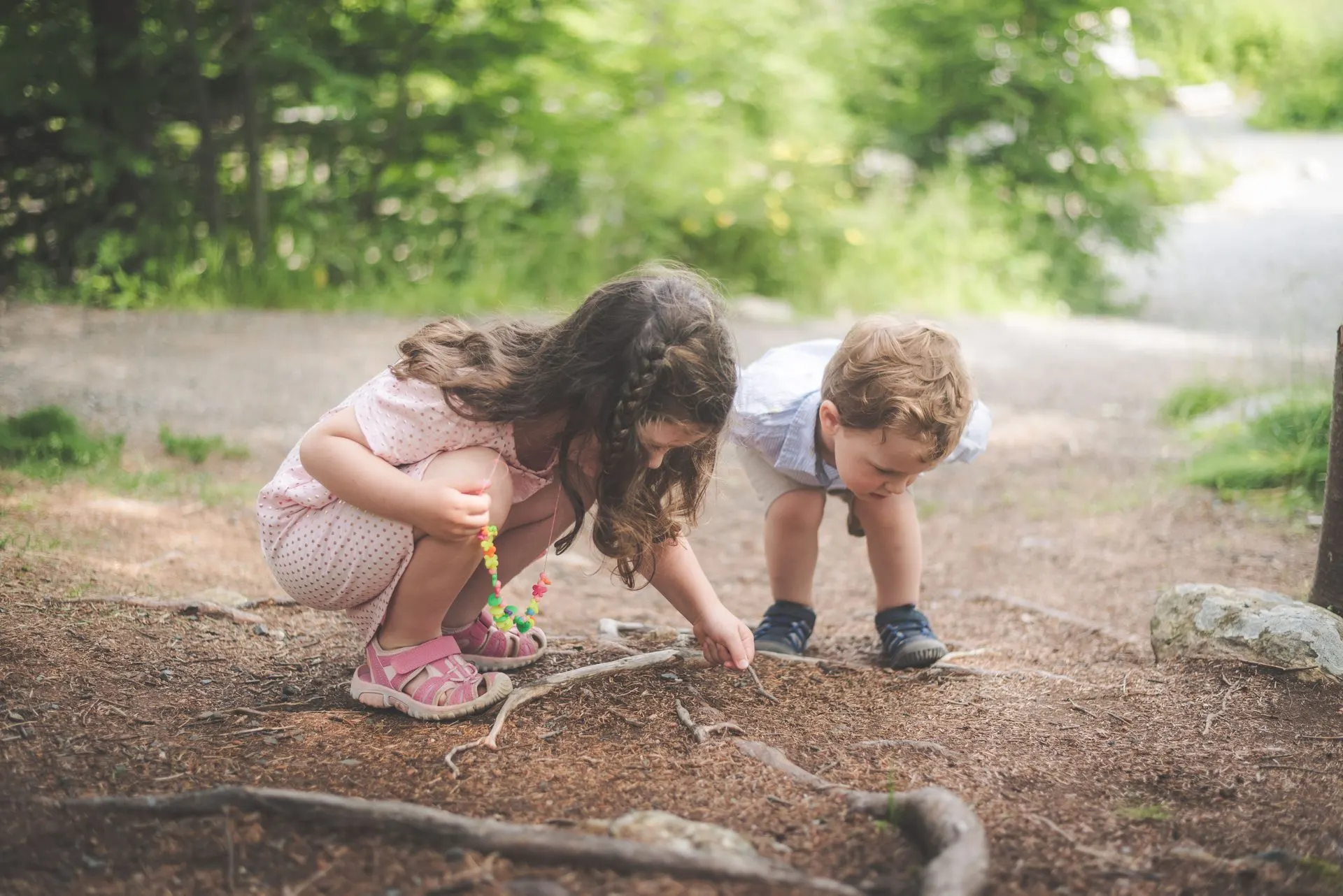 Girl and toddler crouching on a forest path exploring tree roots