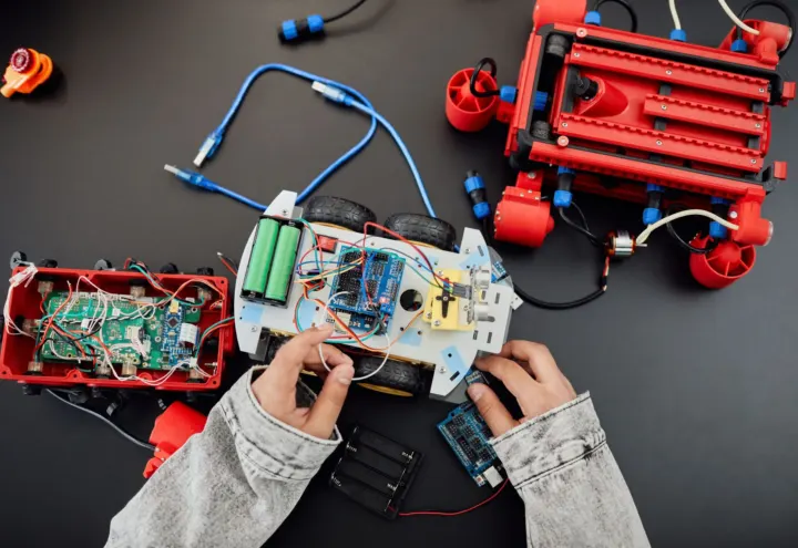 Overhead view of hands assembling a wired robot car among red engineering kit parts
