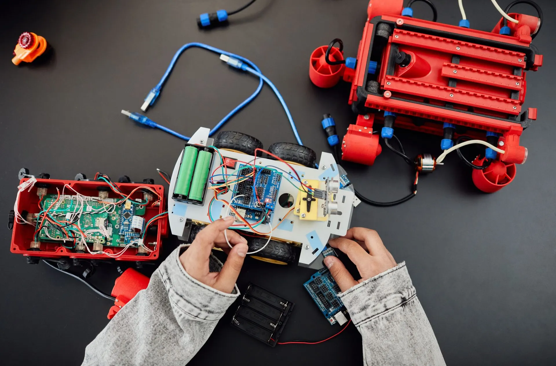 Overhead view of hands assembling a wired robot car among red engineering kit parts