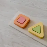 Wooden shape puzzle with pastel square, triangle and circle pieces on light wood
