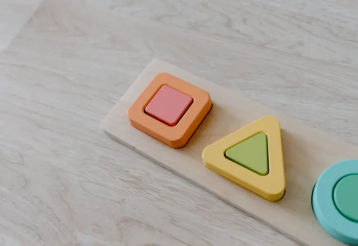 Wooden shape puzzle with pastel square, triangle and circle pieces on light wood