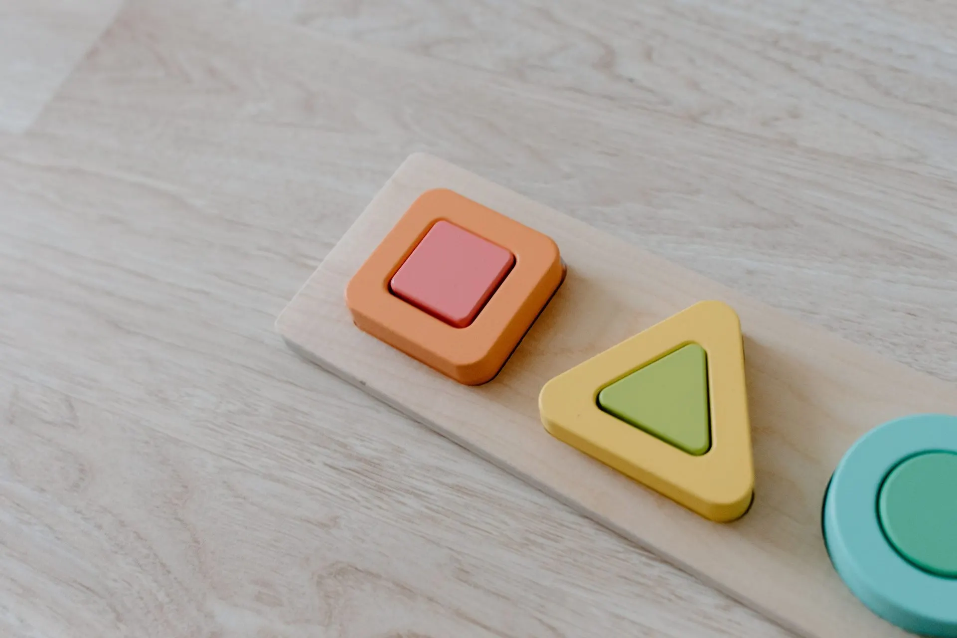 Wooden shape puzzle with pastel square, triangle and circle pieces on light wood