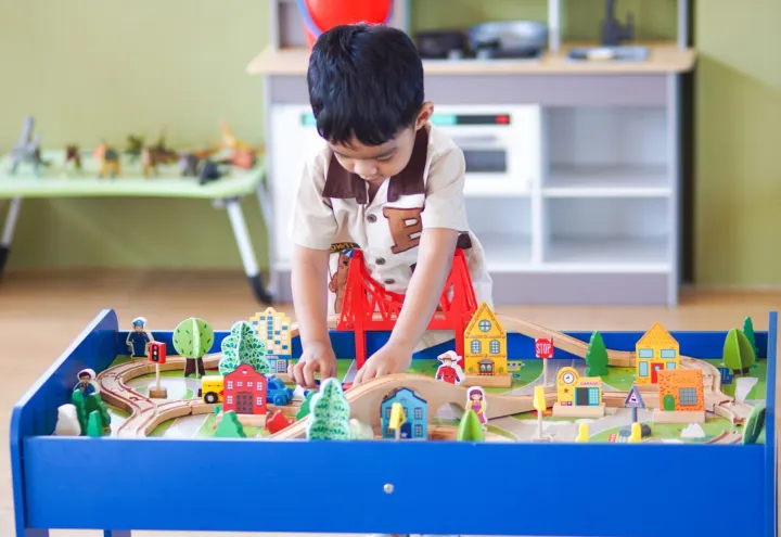 Young boy building a wooden train town with a red bridge