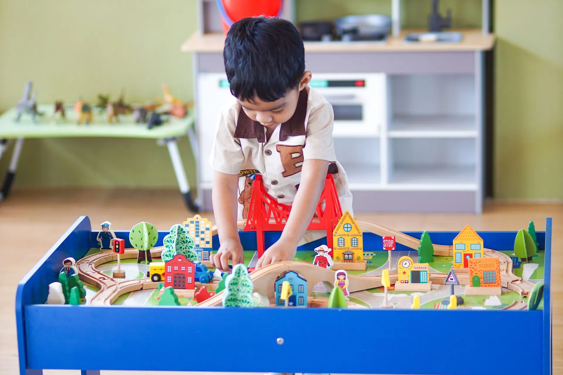 Young boy building a wooden train town with a red bridge